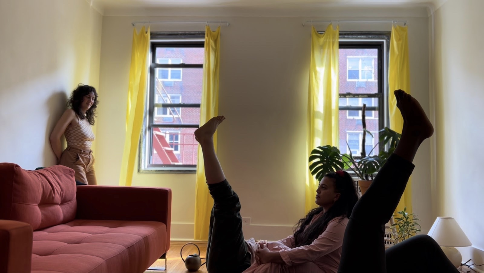 In the final photograph the scene is nearly identical to the image which preceded it. This time the person on their back in the centre of the image and the person at the front around both pointing their legs up to the sky, mirroring each other.